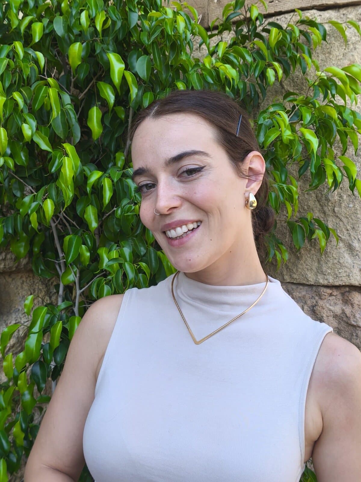 Exshantiva, terapeuta de sonido y tambor chamánico en Madrid, sonriendo frente a una pared de piedra cubierta de hojas